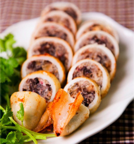 Đập trứng gà vào bột nêm. Trộn đều hỗn hợp. Mực làm sạch để ráo. Sau đó nhồi phần hỗn hợp thịt vào bên trong thân mực. Dùng tăm ghim lại. Cho vào xửng hấp chín. Khi mực nhồi thịt chín, cắt khúc vừa ăn xếp lên đĩa. Trang trí hoa cà chua cùng dưa chuột lên. Ảnh: phunutoday.com.
