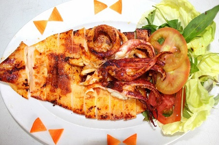 Trộn gia vị vào một chén nhỏ: muối, hạt nêm, tỏi, ớt, ngũ vị hương, dầu mè. Phết đều hỗn hợp gia vị lên mực. Để 3 tiếng đồng hồ cho thấm gia vị vào mực. Nướng mực trên bếp than hoặc loại bếp nướng. Mực rất nhanh chín, nên trong lúc nướng bếp than phải liên tục trở mực để không bị khét. Ảnh: 7monngonmoingay.info.
