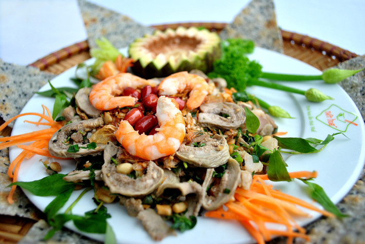 Dùng bao tay trộn tất cả nguyên liệu gồm cả mè và đậu phộng (rau húng quăn cũng được trộn vào, chỉ chừa vài nhánh để trang trí trên mặt đĩa gỏi cho đẹp) cùng chung với phần nước mắm đã chuẩn bị. Sau cùng dọn ra đĩa, rải ớt và rau húng quăn lên. Ảnh: nethue.com.vn.