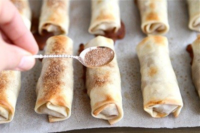 Đánh tan trứng trong 1 chén nhỏ. Sau đó, trải từng lá bánh cuốn lên thớt và dùng cọ quét trứng dọc theo các cạnh. Dùng thìa xúc khoảng 30g nhân táo đặt vào lá bánh. Tiếp đó, lần lượt gấp các cạnh lại rồi khéo léo cuốn thật tròn và chặt tay. Sau đó, bạn đặt bánh táo vào khay nướng đã được lót sẵn giấy nến. Ảnh: monngon.asia.vn.