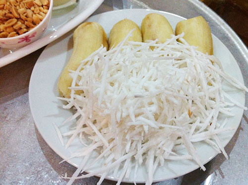 6. Kem chuối lạc. Nguyên liệu: Chuối, sữa chua, nước cốt dừa, sữa đặc, lạc rang giã nhỏ, dừa nạo sợi. Chuối mua về rửa sạch, bỏ vỏ, cắt thành từng lát mỏng theo chiều dọc của quả. Cắt làm 3-5 miếng, tùy theo độ to nhỏ của quả chuối. Cho nước cốt dừa, sữa đặc, sữa chua đã chuẩn bị vào bát, sau đó khuấy đều tay cho hỗn hợp tan đều. Ảnh: Eva.vn.
