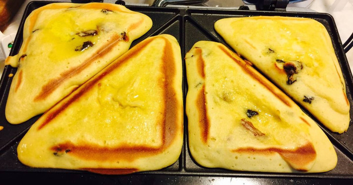 Trộn trái chà là khô, nho khô vào bột đã đánh bông. Nồi hotdog cắm điện và phết lớp bơ rồi dùng thìa canh múc một thìa canh đậy bột cho vào từng khay. Khi xong 4 ô thì đậy lại và khi nó chuyển đèn xanh thì mở nắp, bánh chín. Ảnh: cookpad.com.