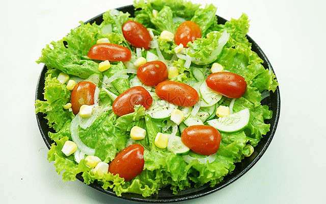 Trộn tỏi ớt với dầu olive, dấm nho, đường, nước mắm trong 1 chén nhỏ. Tưới chén gia vị lên tô xà lách rồi trộn đều bằng tay và hơi bóp nhẹ để rau ngấm gia vị. Rắc ngô và dưa chuột thái lát lên đĩa xà lách là hoàn thành. Ảnh: Cooky.vn.