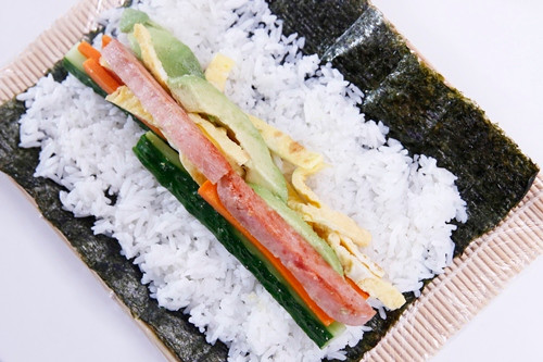 7. Kimbap chiên. Nguyên liệu: Cơm nguội, lá rong biển khô, trứng gà, cà rốt, dưa chuột, xúc xích, ruốc thịt, gia vị, dầu vừng, Trộn cơm với dầu vừng và vừng rang. Đập trứng ra bát, khuấy đều. Tráng trứng chín rồi cắt thành những dải nhỏ 0.5 - 1cm. Dưa chuột, cà rốt thái thành những thanh nhỏ. Xúc xích thái miếng dài bằng cà rốt. Ảnh: eva.vn.
