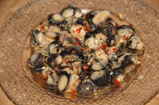 2. Ốc xào chuối xanh. Nguyên liệu: Ốc bươu, chuối xanh, lá lốt, lá tía tô, ớt sừng đỏ, mỡ heo, lạc rang sẵn. Gia vị: Hành khô, tỏi, bột nghệ, muối, hạt nêm, bột ngọt, tiêu, ớt bột, dầu ăn. Hành khô, tỏi: Làm sạch, băm nhỏ; Ớt sừng: Bỏ cuống, rửa sạch, 3 trái thái lát, 5 trái băm nhỏ. Ngâm ốc vào nước có pha với 5 trái ớt sừng băm nhỏ trong 30 phút cho thật sạch nhớt. Lấy thịt ốc ướp với ½ hành khô, tỏi băm nhỏ, hạt nêm, bột ngọt, bột nghệ, ớt thái lát, dầu ăn, tiêu, ớt bột trong 20 phút. Ảnh: toinayangi.vn.