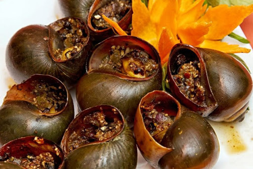 4. Ốc nướng nước mắm. Nguyên liệu: Ốc bươu, nước mắm, tỏi băm, gưng băm, tiêu, đường. Ốc bươu đem về rửa sạch bên ngoài, cho vào chậu ngâm với nước có một trái ớt được đập giập để nhả nhớt trong 2 giờ. Gừng băm, tỏi băm vắt nước hoà với nước mắm, đường và tiêu. Cho hỗn hợp này vào từng con ốc ướp khoảng 15 phút. Sau đó nướng trên lửa than. Ảnh: diendanamthuc.com.