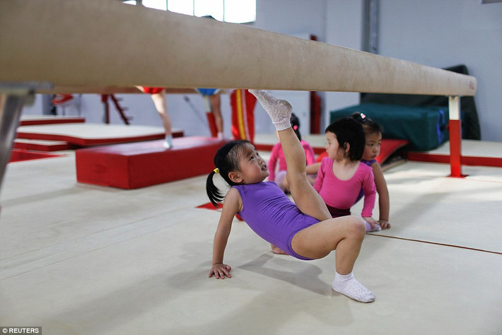 Bé gái đang cố vươn chân cao trong một tư thế của thể dục dụng cụ.
