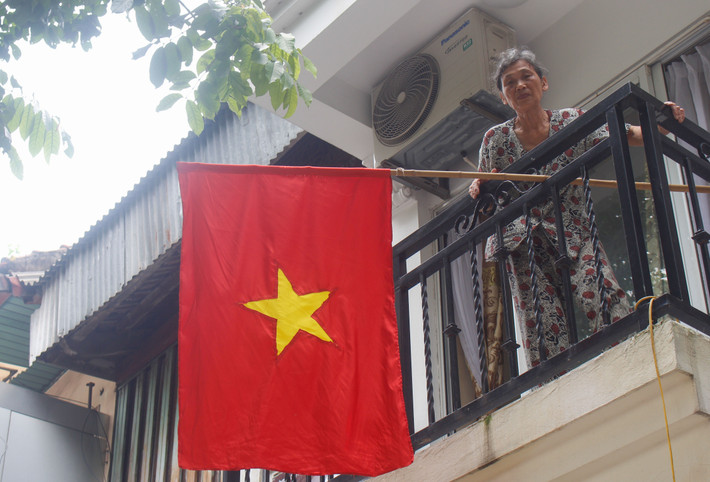 Một cụ già chỉnh trang lại lá cờ Tổ quốc trên phố Hàng Bài.