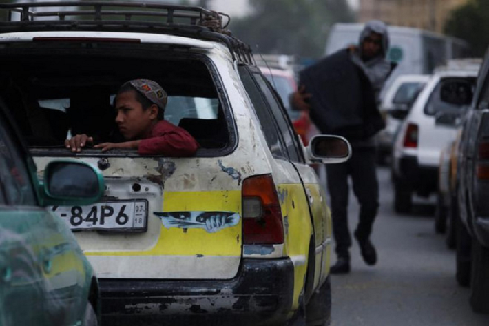 Cậu bé người Afghanistan ngồi sau chiếc xe hơi đang di chuyển trên đường phố