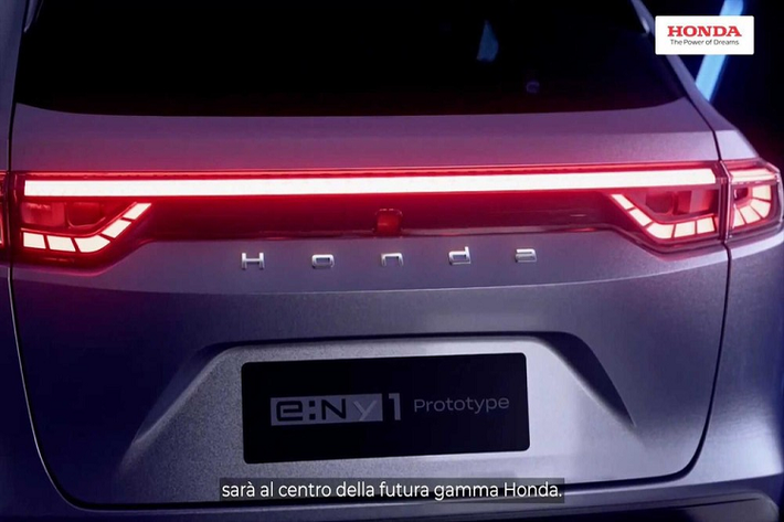 Nhìn từ hai bên, Honda e:Ny1 có đường gân nổi giữa chạy dọc hết chiều dài thân xe, bộ lazăng đa chấu được mạ crôm bóng khá bắt mắt. Tay nắm cửa sau có vẻ như được bố trí tích hợp trênk hung cửa sổ.