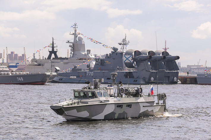 Tàu tuần tra cao tốc Project 03160 Raptor đang chạy về địa điểm neo đậu để trưng bay. Bên cạnh tàu tuần tra còn có nhiều chiến hạm khác, bao gồm cả loại tàu đổ bộ đệm khí cỡ lớn.