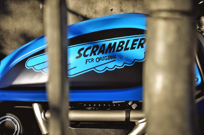Ốp bình xăng được sơn đen, sau đó vẽ logo Scrambler màu xanh lên.
