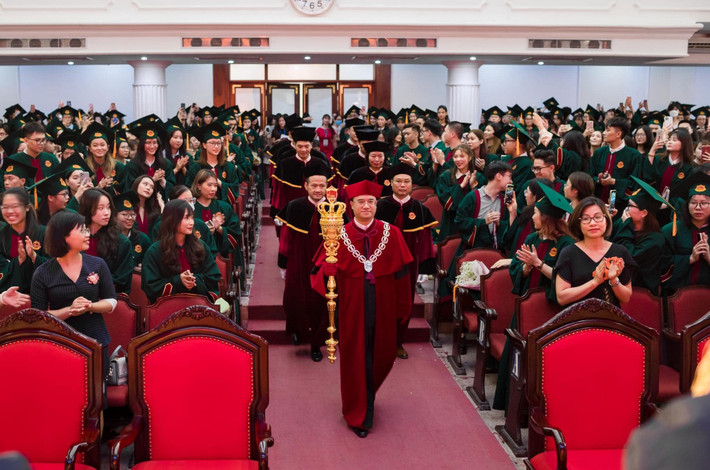 PGS.TS Nguyễn Trúc Lê - hiệu trưởng Trường Đại học Kinh tế mặc áo choàng nhung đỏ, đội mũ đỏ và đi găng tay đồng màu, cầm quyền trượng màu vàng và mang vòng cổ lớn màu trắng trong buổi lễ trao bằng tốt nghiệp chính quy.