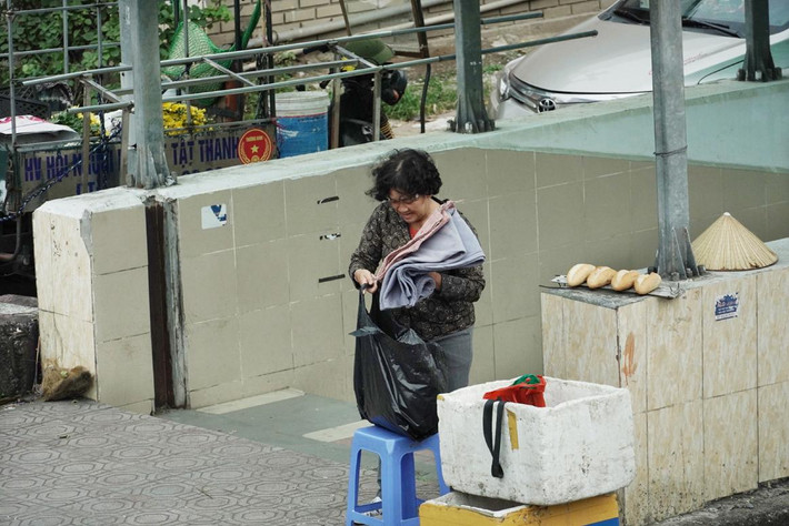 Bà bán bánh mì trước cửa hầm đường bộ Ngã Tư Sở đang cất vào túi cái chăn nhỏ mà sáng sớm mình vừa sử dụng.