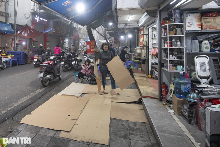 Một chủ kinh doanh trên phố Hàng Khoai phải dùng những tấm bìa để trải trước vỉa hè do nồm ẩm gây trơn trượt (Ảnh: Mạnh Quân).