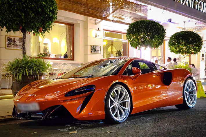 Chiếc McLaren Artura tại Sài Gòn này sở hữu màu sơn ngoại thất đỏ cam nổi bật, đi cùng một số chi tiết được sơn đen tương phản. Cách thiết kế của xe cũng mang đậm tính khí động lực học và đặc trưng của các mẫu xe hiệu suất cao. Artura được trang bị bộ mâm Dynamo 10 chấu siêu nhẹ, sơn đen bóng, đi cùng cùm phanh tone sur tone màu đen.