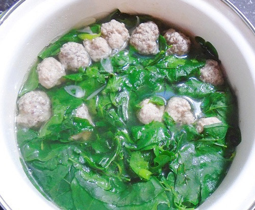 Đun sôi nồi nước trên bếp, thả từng viên thịt vào nấu chín rồi vớt ra đĩa. Phi thơm hành cùng chút dầu ăn, cho rau vào đảo đều, chín tới. Cho phần nước vừa luộc thịt vào nồi rau, đun sôi trở lại thì cho thịt viên vào, nêm nếm lại gia vị cho vừa miệng rồi tắt bếp, mở vung cho canh nguội bớt. Ảnh: phunutoday.vn.