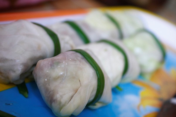 Lá bắp cải cắt bớt sống lá, chần sơ qua nước sôi cho mềm. Hành lá tách từng cọng, nhúng sơ qua nước sôi. Trải 1 lá bắp cải ra đĩa, cho thịt vào giữa, cuộn lại và cột bằng hành lá.