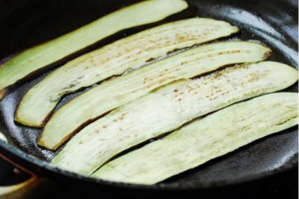 3. Cà tím cuộn ngũ sắc. Nguyên liệu: Cà tím, dầu ăn, sốt mayonnaise, tỏi, tôm, ớt chuông, tăm. Dùng dao sắc cắt cà tím thành những lát mỏng theo chiều từ cuống xuống. Làm nóng chảo trên bếp với chút dầu ăn vào, cho từng lát cà vào chiên đến nào cà có màu vàng nâu thì lấy ra đĩa, để riêng. Ảnh: Monngon.tv.