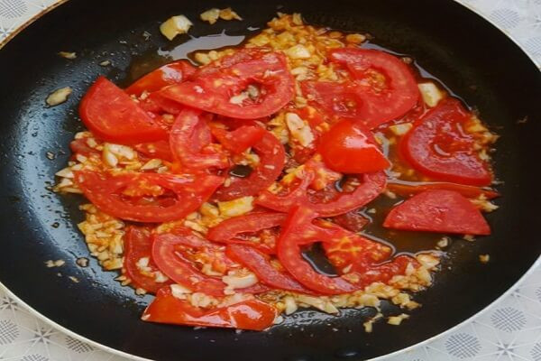 Gạn lấy nước trong để nấu canh. Nặn sạch đầu đen của trai, rửa sạch thái nhỏ ướp với nhánh gừng rửa sạch đập dập băm nhỏ cùng thìa bột nêm. Cho thìa dầu vào phi thơm hành khô cho trai và cà chua vào xào, cho bột nêm đảo đều cho ngấm. Ảnh: monngon.tv.