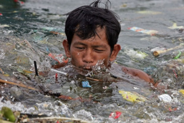 Một người đàn ông bơi qua rác ở vịnh Manila, Philippines
