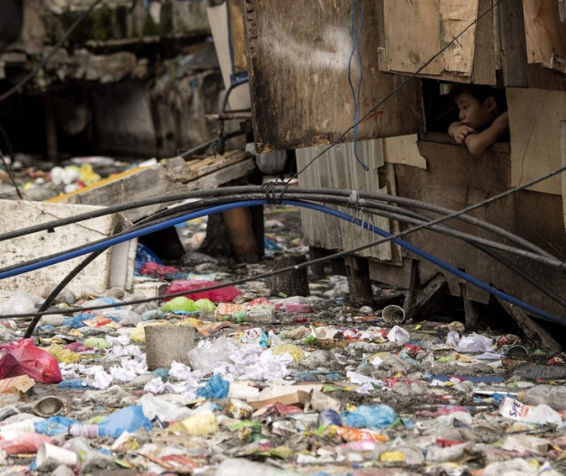 Cậu bé nhìn qua cửa sổ ngôi nhà cạnh bãi rác ở Manila