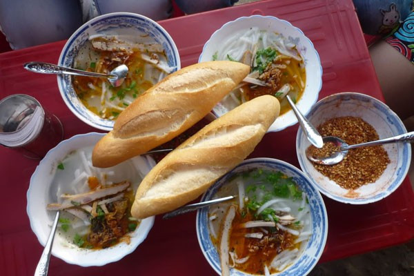 Bánh canh chờ tại Đà Nẵng. Không chỉ như tên gọi là phải “chờ” mới được ăn, khi bạn đến đây phải sẵn sàng tầm lý “tự phục vụ” nếu không muốn mang cái bụng đói ra về. Tuy vậy, có lẽ chẳng ai thấy phiền lắm vì bánh canh chờ “vừa ngon vừa rẻ”. Quán ở cuối đường Trần Hưng Đạo, bàn ghế đơn sơ được đặt trên dải đất trống, muốn ăn cũng phải tự phục vụ từ tô cháo đến bánh mì và giá chỉ 7.000đ/ tô. (Ảnh: dulichdanang.vn).