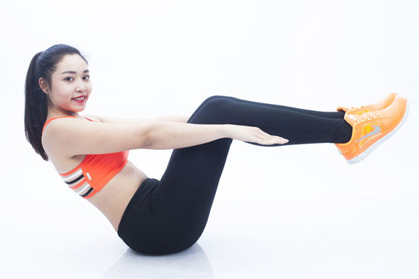Giữ gập bụng cố định: Bắt đầu bằng tư thế nâng chân và lưng khỏi sàn. Cẳng chân song song với mặt sàn, thân cuộn tròn. Hai tay chạm nhẹ vào đầu gối để giữ thăng bằng.