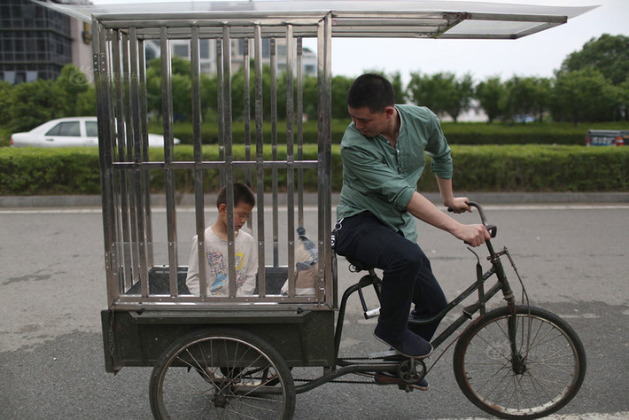 Tiểu Hào là một cậu bé năm nay 10 tuổi, ở Thái Châu, Chiết Giang, Trung Quốc. Không giống như bạn bè cùng trang lứa, Tiểu Hào không thể tự chăm sóc mình bởi căn bệnh bại não quái ác. Trong ảnh: Cha Tiểu Hào nhốt con trong cũi đưa đi chơi.