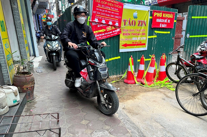 Người dân đi bộ và xe máy luồn hàng rào công trường để đi lại.