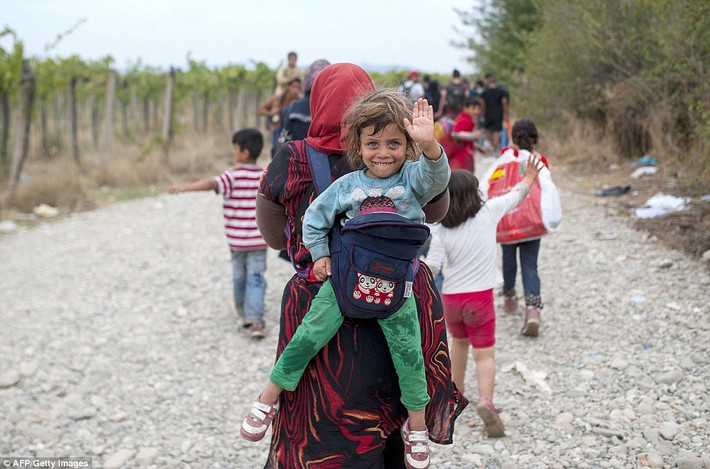 Bé gái được mẹ cõng trên lưng khi gia đình em đi qua biên giới Hy Lạp và Macedonia. (Nguồn: Dailymail).
