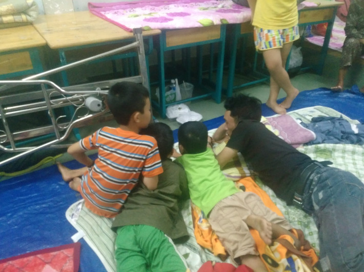 Người đàn ông cùng các cháu nhỏ nằm trên tấm bạt vui vẻ cùng nhau xem phim qua điện thoại.