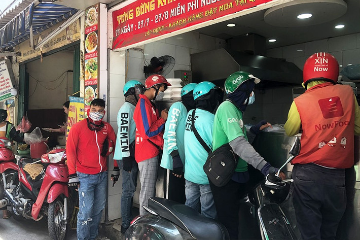 Tại một cửa hàng bún bò tại phố Nghĩa Tân, ngay khi thông báo có đơn trên app, các nhân viên sẽ chuẩn bị đồ và chuyển ra chiếc bàn ngay lối ra vào. Việc này vừa giúp giữ khoảng cách giữa nhân viên cửa hàng với các shipper, vừa đảm bảo các shipper không phải xếp hàng đợi lâu.