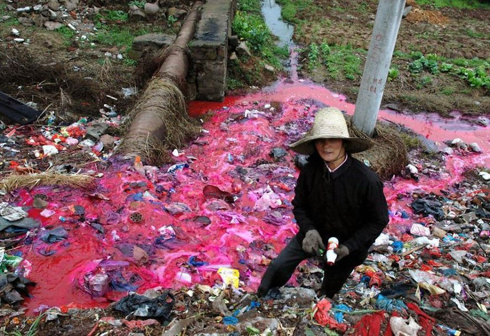 Một người phụ nữ đang thu thập chai nhựa gần con sông bị ô nhiễm nặng.