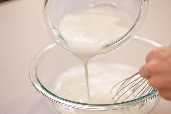 B2. Sau đó bạn cho toàn bộ sữa tươi và lá glatin đã mềm vào trong nồi (khoảng 500 ml) cùng với sữa đặc, sữa milo để lên bếp đun nóng khoảng 45-50độ C và không để hỗn hợp sôi ngoáy thật đều. Bạn đổ sữa chua vào nồi sữa tươi và sữa đặc ở trên sau đó khuấy thật đều để hòa tan hoàn toàn hỗn hợp quyện vào với nhau. Ảnh. Agiadinh.