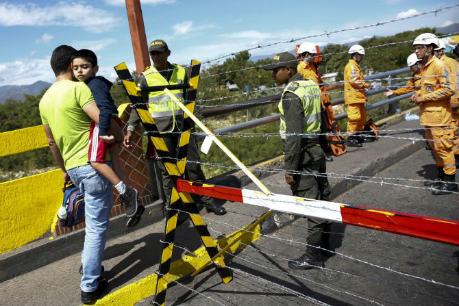Một người đàn ông bế con trai đi trên cây cầu Simon Bolivar, San Antonio để trở về Colombia ngày 26/8.