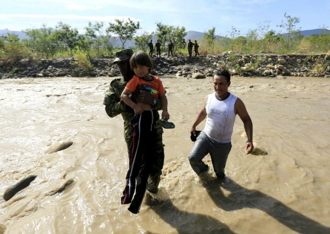 Một cảnh sát Colombia bế em nhỏ qua sông Tachira ngày 26/8.