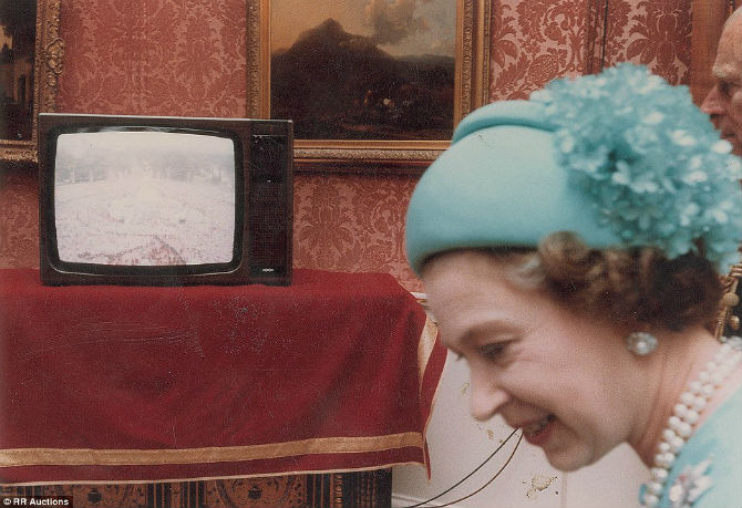 Nữ hoàng Elizabeth II đứng trước chiếc TV đang tường thuật khung cảnh bên ngoài cung điện Buckingham.