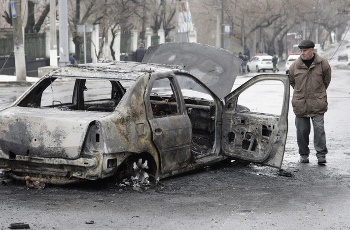 Người đàn ông quan sát chiếc xe ô tô bị cháy rụi gần bến dừng xe buýt ở Donetsk, Ukraine ngày 22/1/2015.