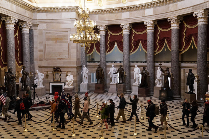Người biểu tình đem theo cờ và băng rôn ủng hộ ông Trump tiến vào sảnh của Điện Capitol. Ảnh: New York Times.