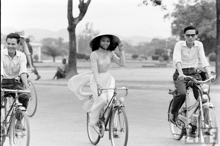 Thiếu nữ áo dài Huế tươi tắn khi đạp xe bên các đấng mày râu, 1961. Ảnh: Life.