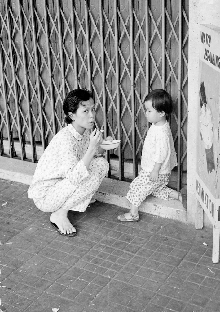 Bà mẹ bón cơm cho con gái trên vỉa hè. Ảnh: Vietnam Center and Archive.