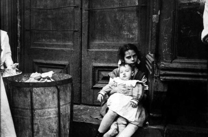 Hai chị em ngồi cạnh thùng rác trước cửa nhà. Ảnh: Jacob Riis.