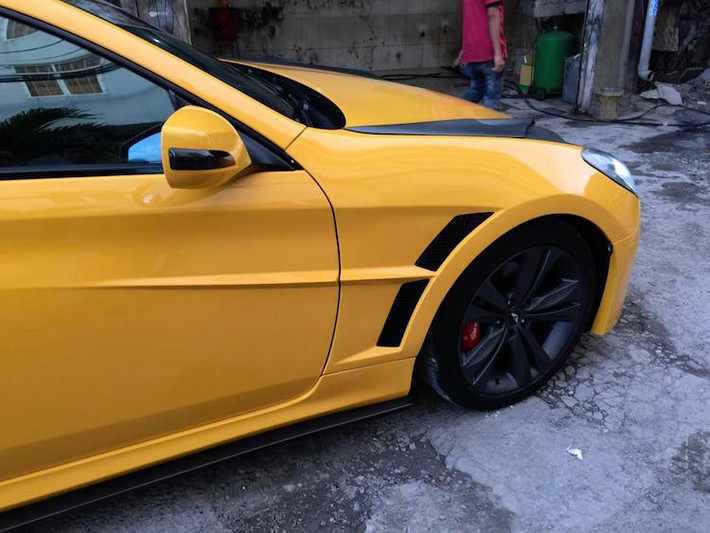 Vè trước của Genesis cũng được "trổ" thêm những khe tản nhiệt tương tự như trên Aston Martin One-77 thật. Mâm gốc của Genesis chỉ được sơn lại màu đen mờ khỏe hơn.