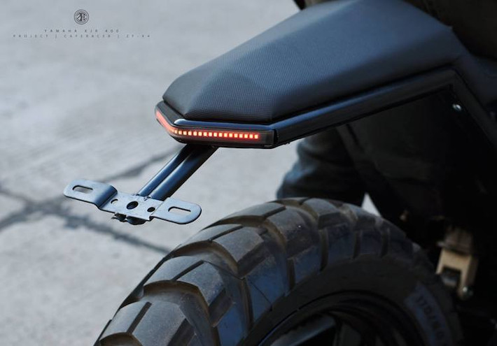 Ở phía sau, phần khung phụ và lườn của XJR400 đã được ZIFE Design thay đổi hoàn toàn, với vẻ ngoài góc cạnh hơn. Theo phong cách thường thấy của xưởng độ, bộ yên xe cũng đã được cắt gọn tỉ mỉ thành những bề mặt phẳng, góc cạnh. Nằm phía sau đuôi xe là cụm đèn hậu LED nằm gọn bên trong khung phụ.