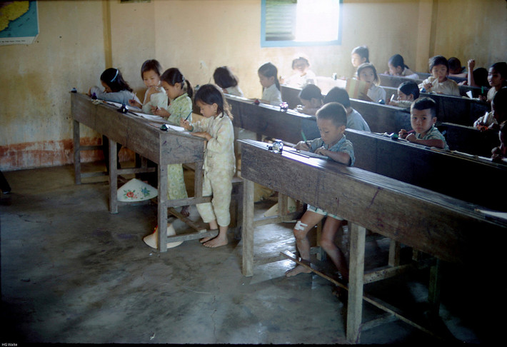 Những đứa trẻ phải đứng để viết bài do bàn ghế quá cỡ. Ảnh: Smugmug.com.