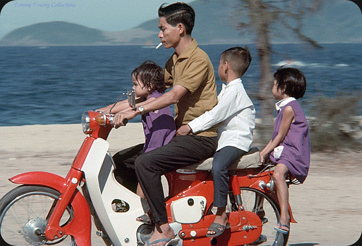Người đàn ông và ba em bé trên chiếc Honda Dame C50 màu đỏ.