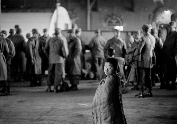 Một cậu bé đứng gần nhóm binh sĩ ở nhà ga Busan. Ảnh: Werner Bischof.