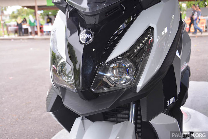 So với bản concept, SYM CruiSYM 300i đã có khá nhiều sự thay đổi. Ở phía trước, cũng giống như MAXSYM 500, CruiSYM 300i cũng sở hữu cặp đèn pha kép với 2 bóng pha dạng thấu kính projector và đèn chiếu sáng ban ngày LED. Tuy nhiên so với MAXSYM, cụm đèn pha của xe đã có thiết kế khá khác biệt với kích thước to hơn, nhưng ít sắc sảo hơn.
