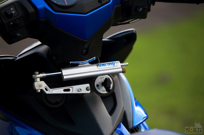 Ở bên dưới cổ xe, một cây trợ lực Ohlins đã được gắn thêm một cách khéo léo vào Exciter bằng pát "thửa riêng" và khoét nhựa gáy của xe. Cùng với cặp bánh lớn, trợ lực lái khiến cảm giác điều khiển của chiếc xe trở nên càng đầm chắc hơn.